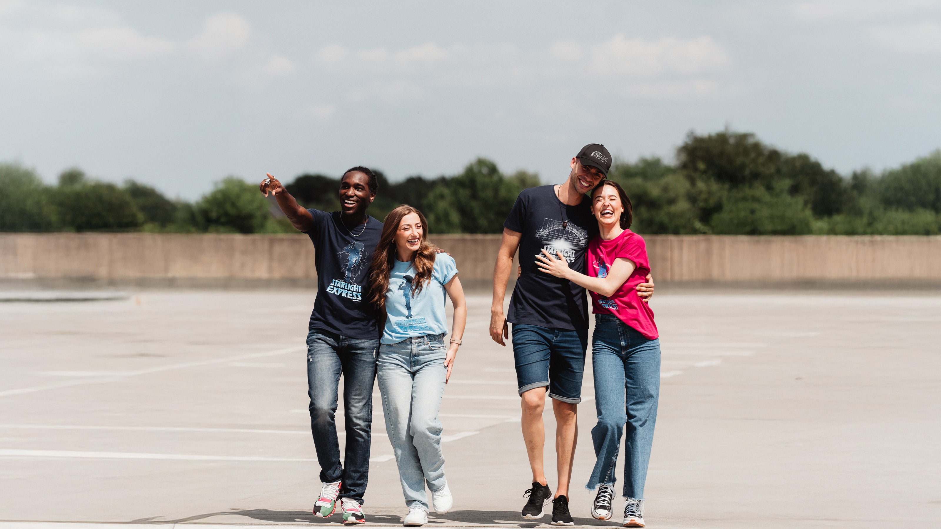Zwei Pärchen schlendern fröhlich gelaunt und paarweise eng umarmt über einen Parkplatz und tragen dabei unterschiedliche T-Shirts mit Starlight Express Motiven aus diesem Shop.