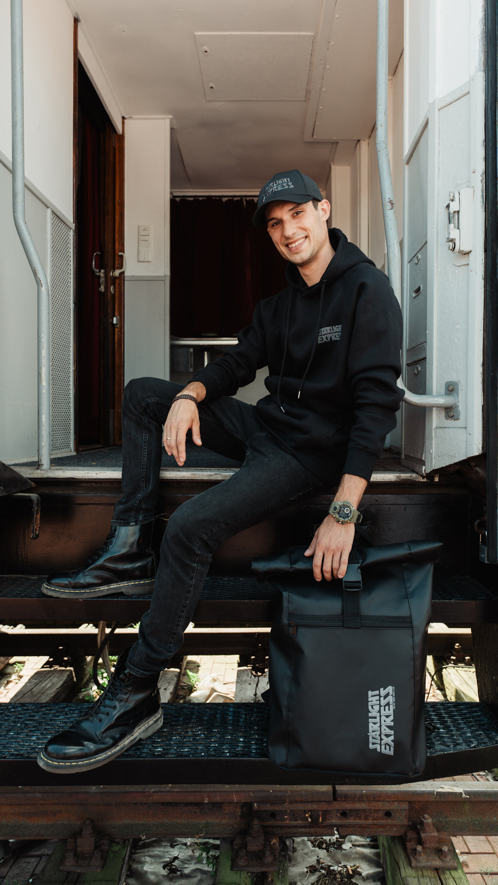 Ein Mann sitz auf einer Treppe und neben ihm steht der schwarze Rucksack als LKW-Plane mit Starlight Express Logo.