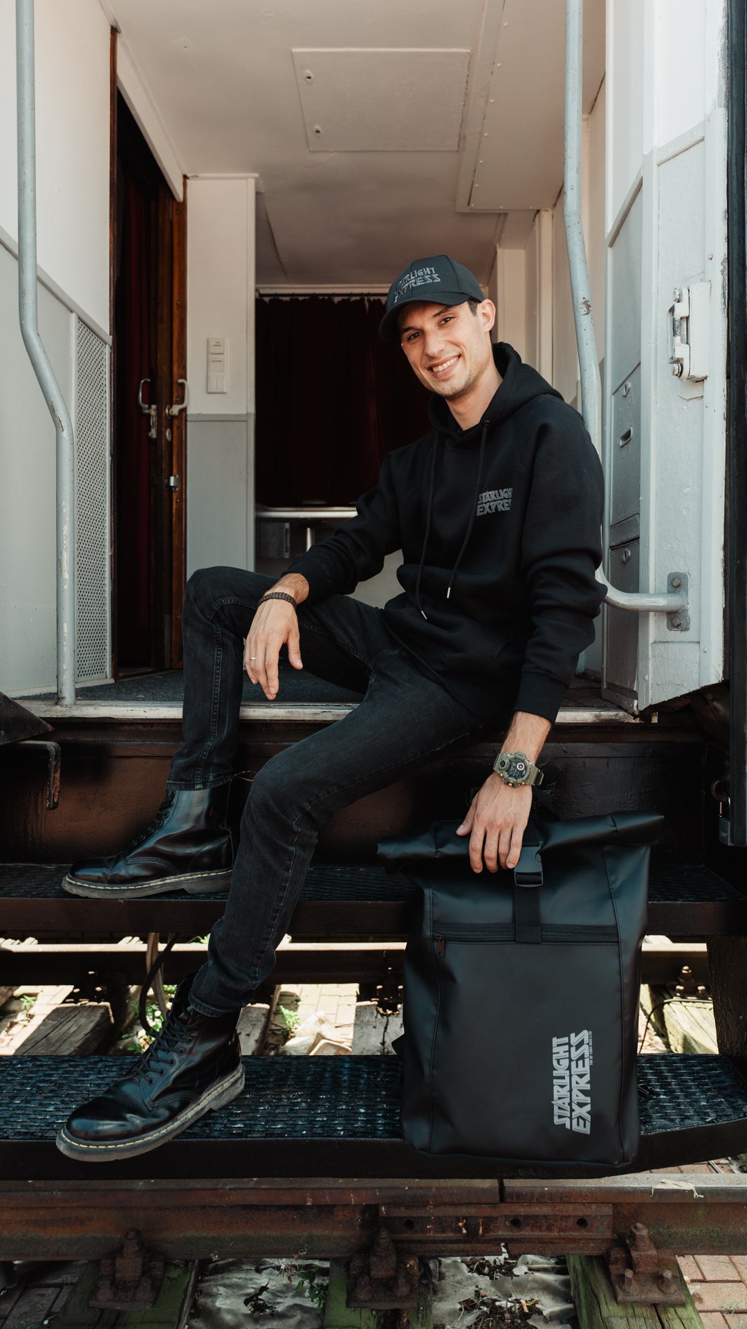 Ein Mann sitz auf einer Treppe und neben ihm steht der schwarze Rucksack als LKW-Plane mit Starlight Express Logo.